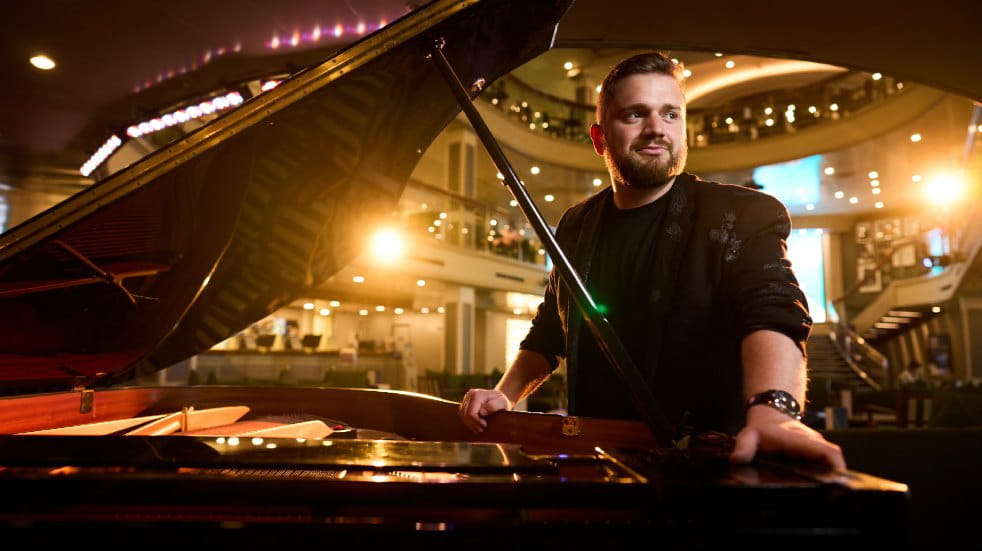 Callum Bradley standing by his piano on board Ambassador's ship Ambience. Credit: Joby Sessions